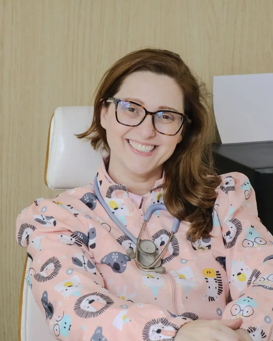 Dra. Cintia Urel em seu consultório, com jaleco estampado de bichinhos